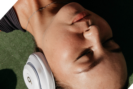 Close-up of a young woman resting her head, eyes closed and expression relaxed, wearing white headphones.