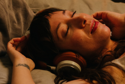 Close-up of a young woman with black hair resting her head, eyes closed and expression relaxed, wearing red headphones.